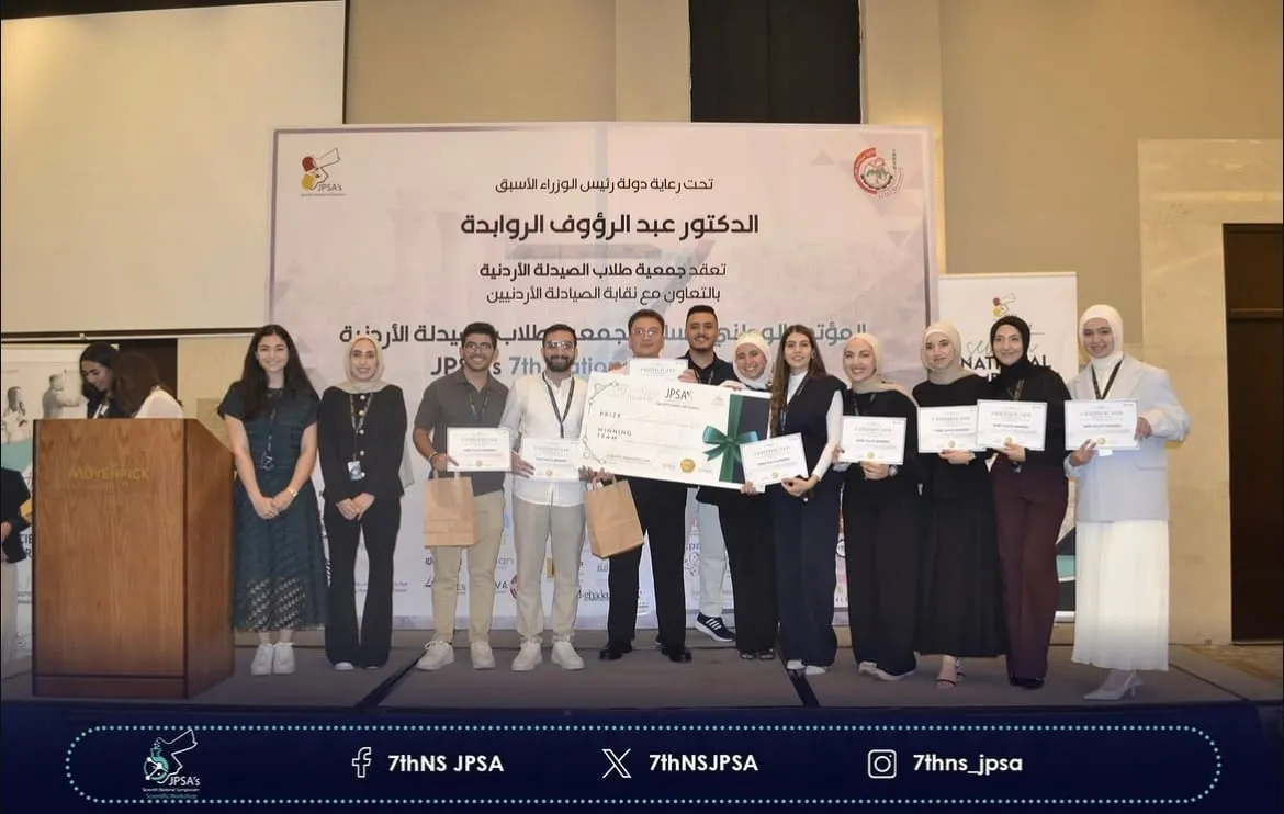 A group on stage holding certificates and an oversized cheque, in front of the symposium backdrop