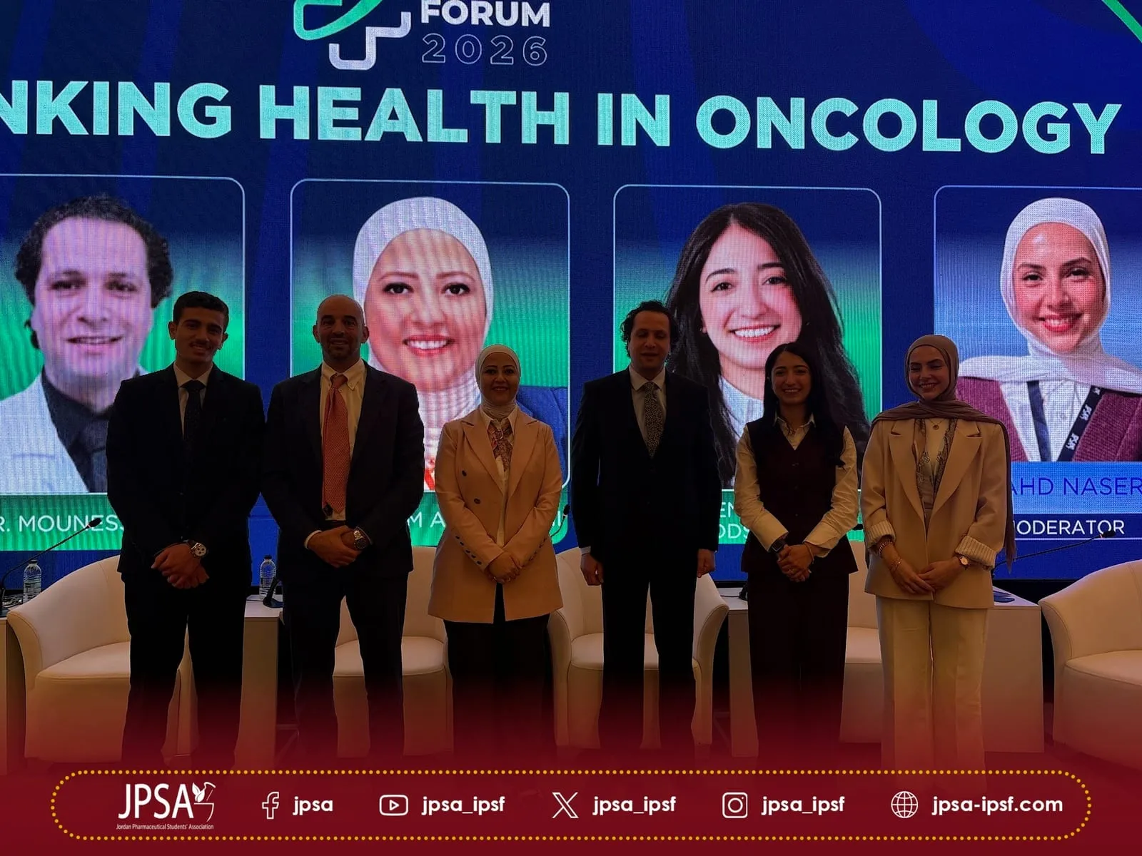 Six people posing on stage in front of the panel screen
