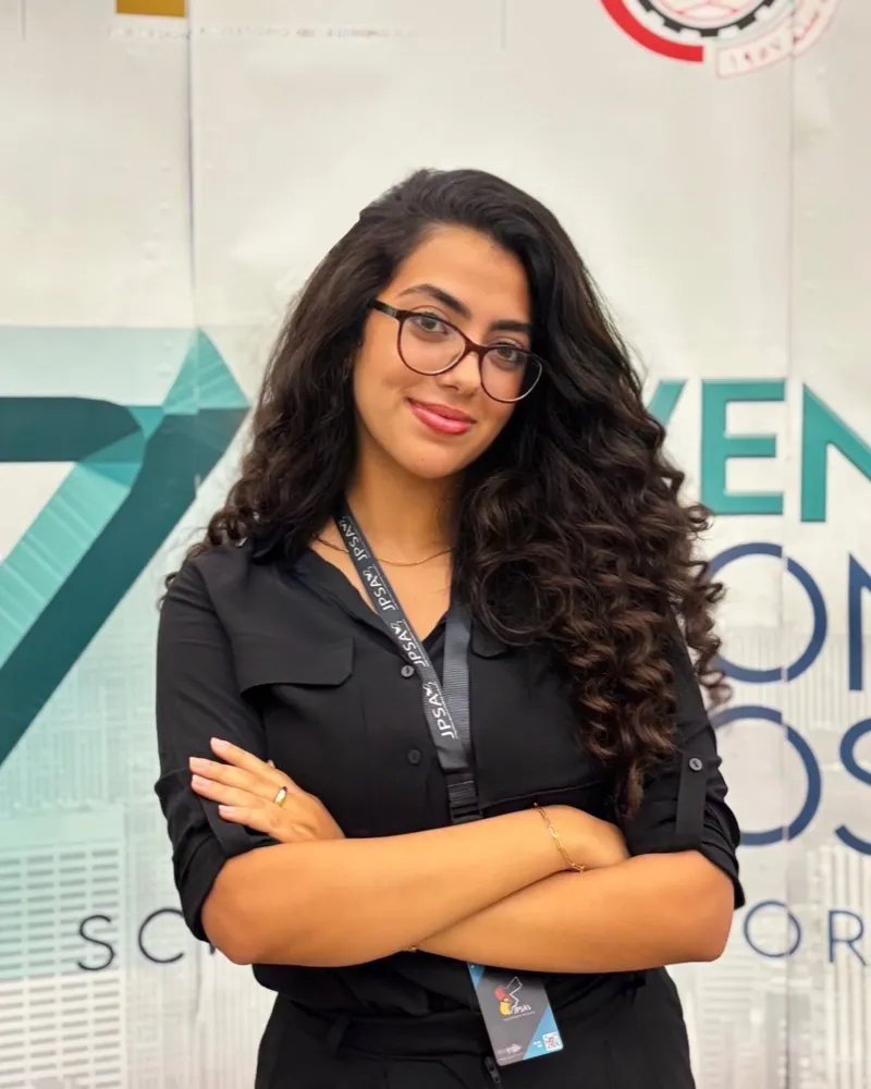 A JPSA member with arms crossed in front of the 7th National Symposium banner