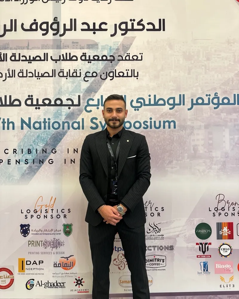 A JPSA member in a suit in front of the 7th National Symposium backdrop