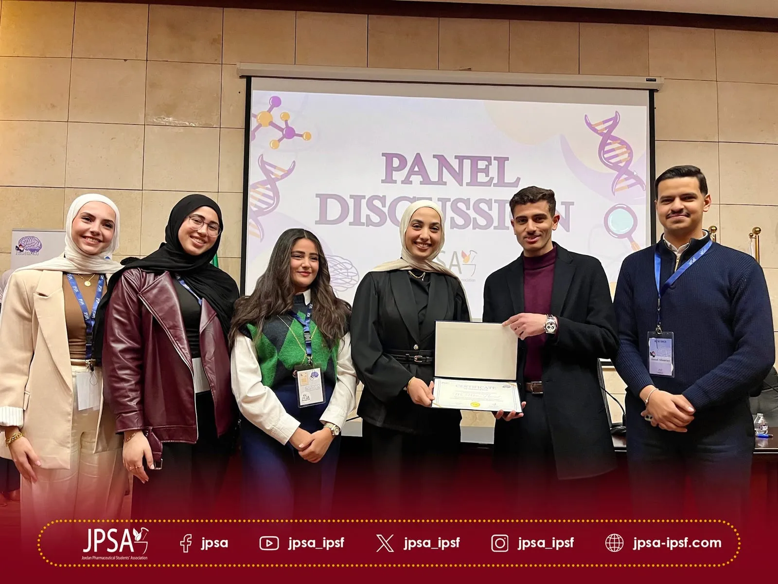 A group holding a certificate, in front of a panel discussion slide