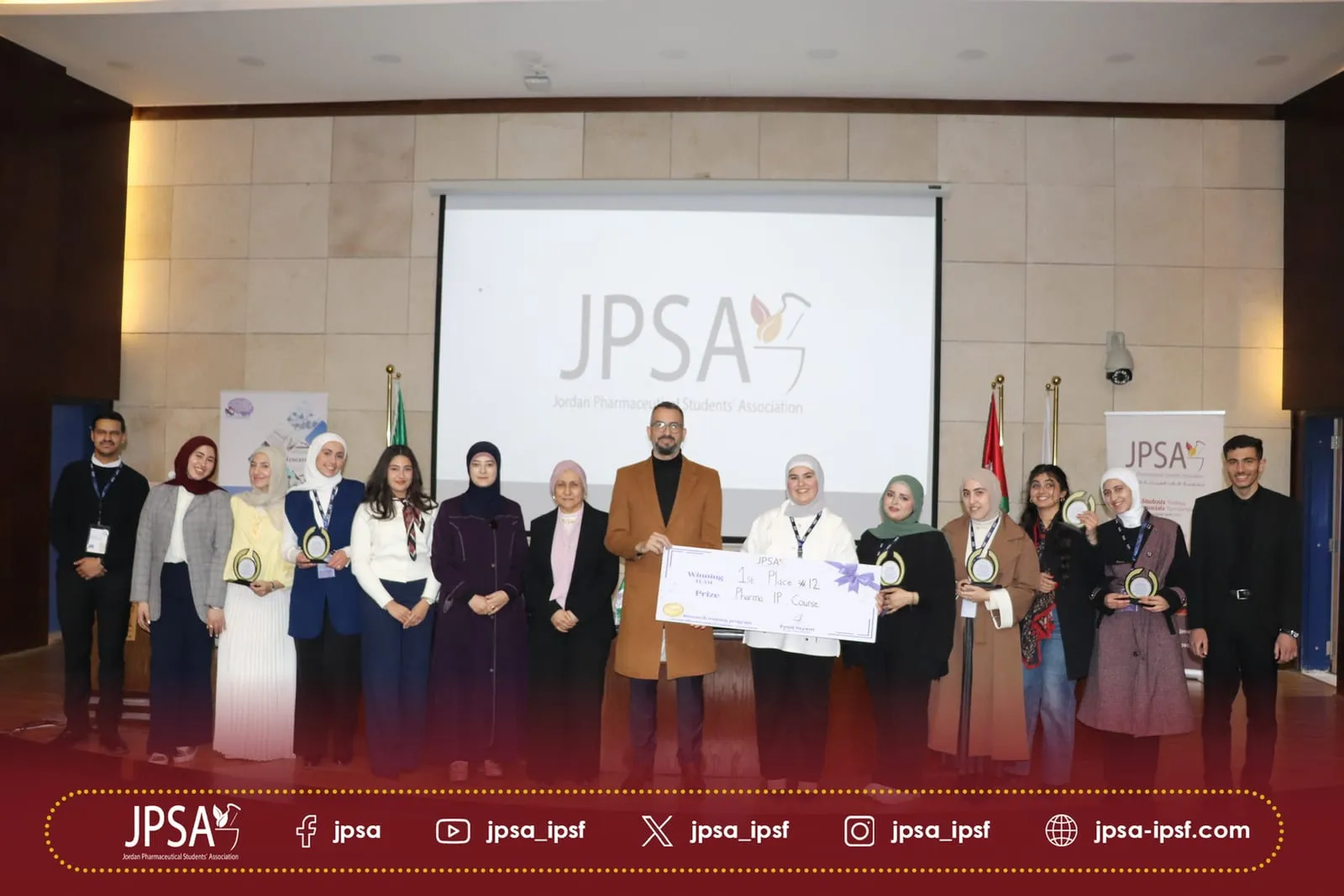 A large group on stage in front of the JPSA logo, holding awards and an oversized cheque