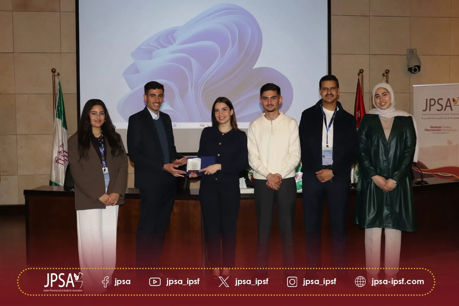 An award handed over on stage, beside a JPSA banner